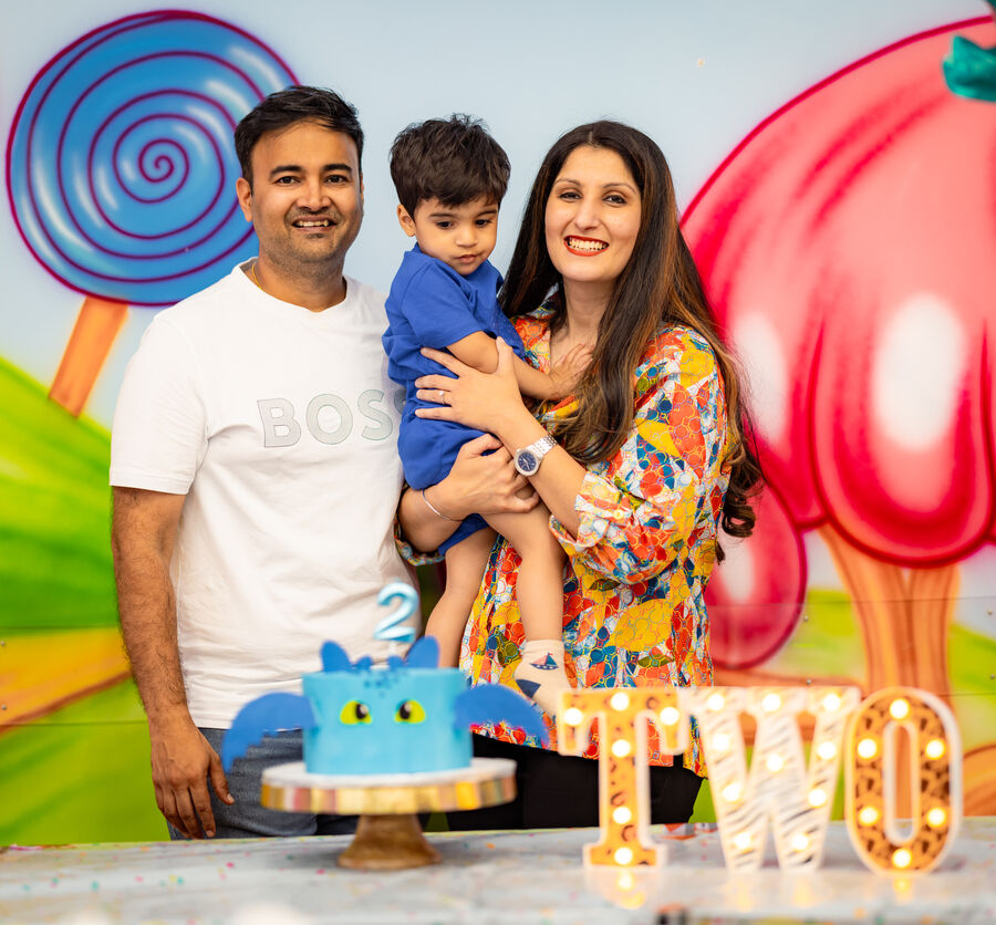 Parents holding their son beside a dragon cake at his second birthday party