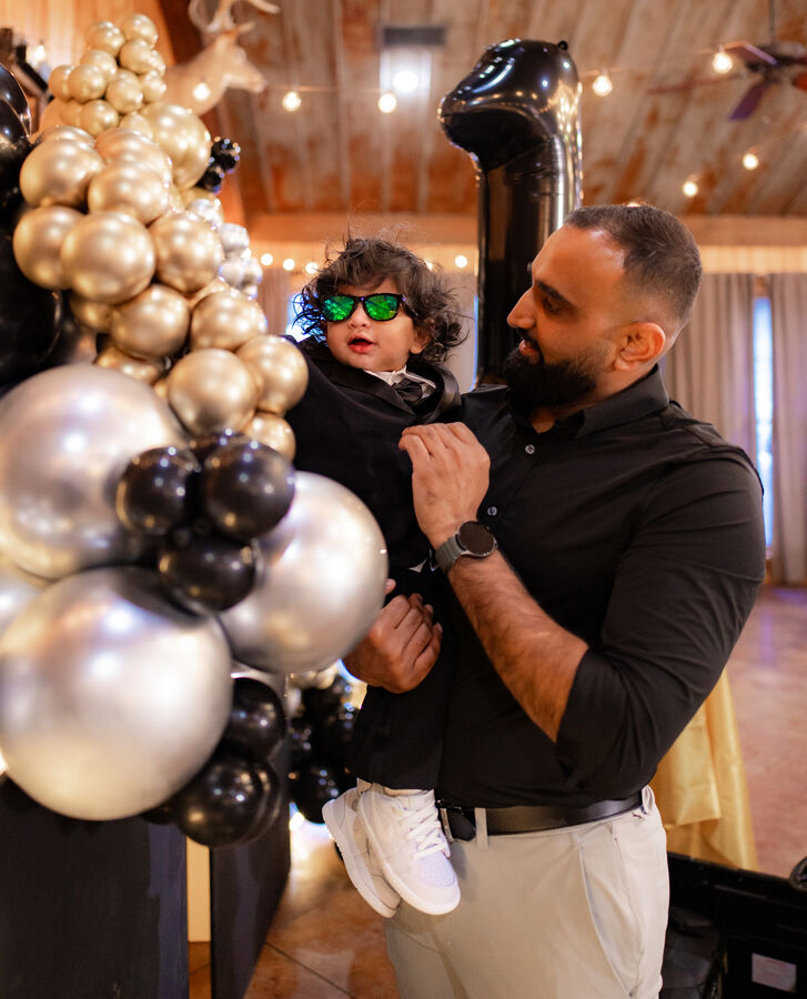 Father holding his toddler son wearing sunglasses at a birthday celebration