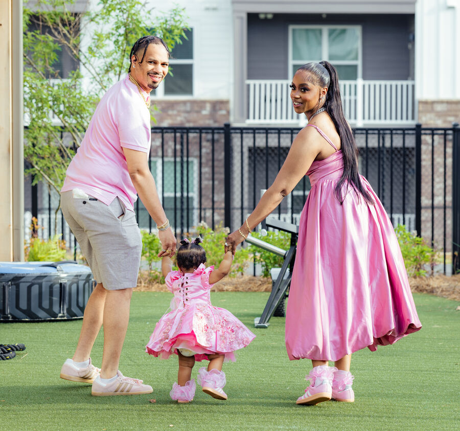 Parents in pink walking with their baby daughter at an outdoor birthday shoot