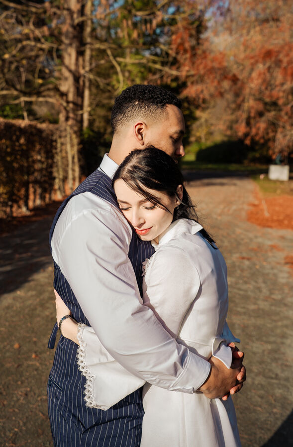 Couple hugging on a sunlit park path during their engagement shoot