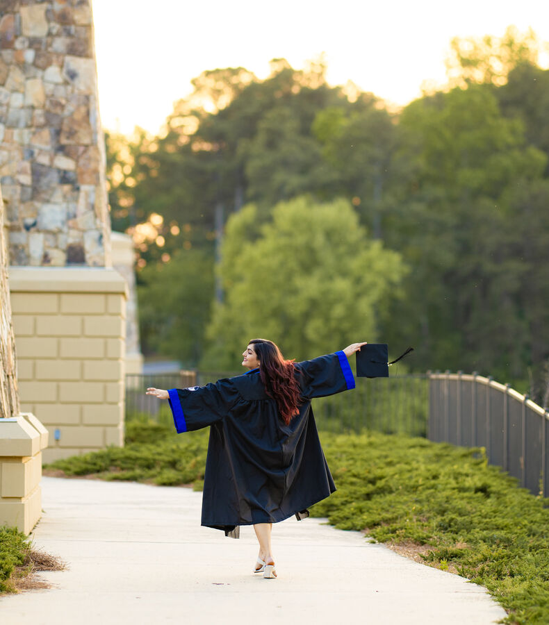 Graduate spinning in her gown with cap in hand at golden hour