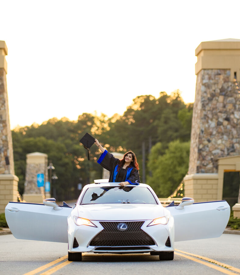Graduate waving her cap from the sunroof of a white car